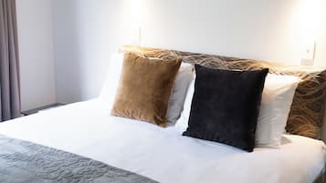 A neatly made bed with a patterned throw, two wall-mounted reading lights, and a window with curtains.
