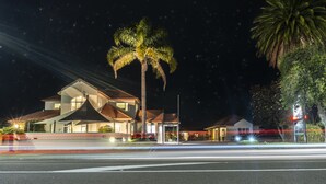 Una casa moderna de dos pisos con un balcón grande, una palmera y una calle con estelas de luz.