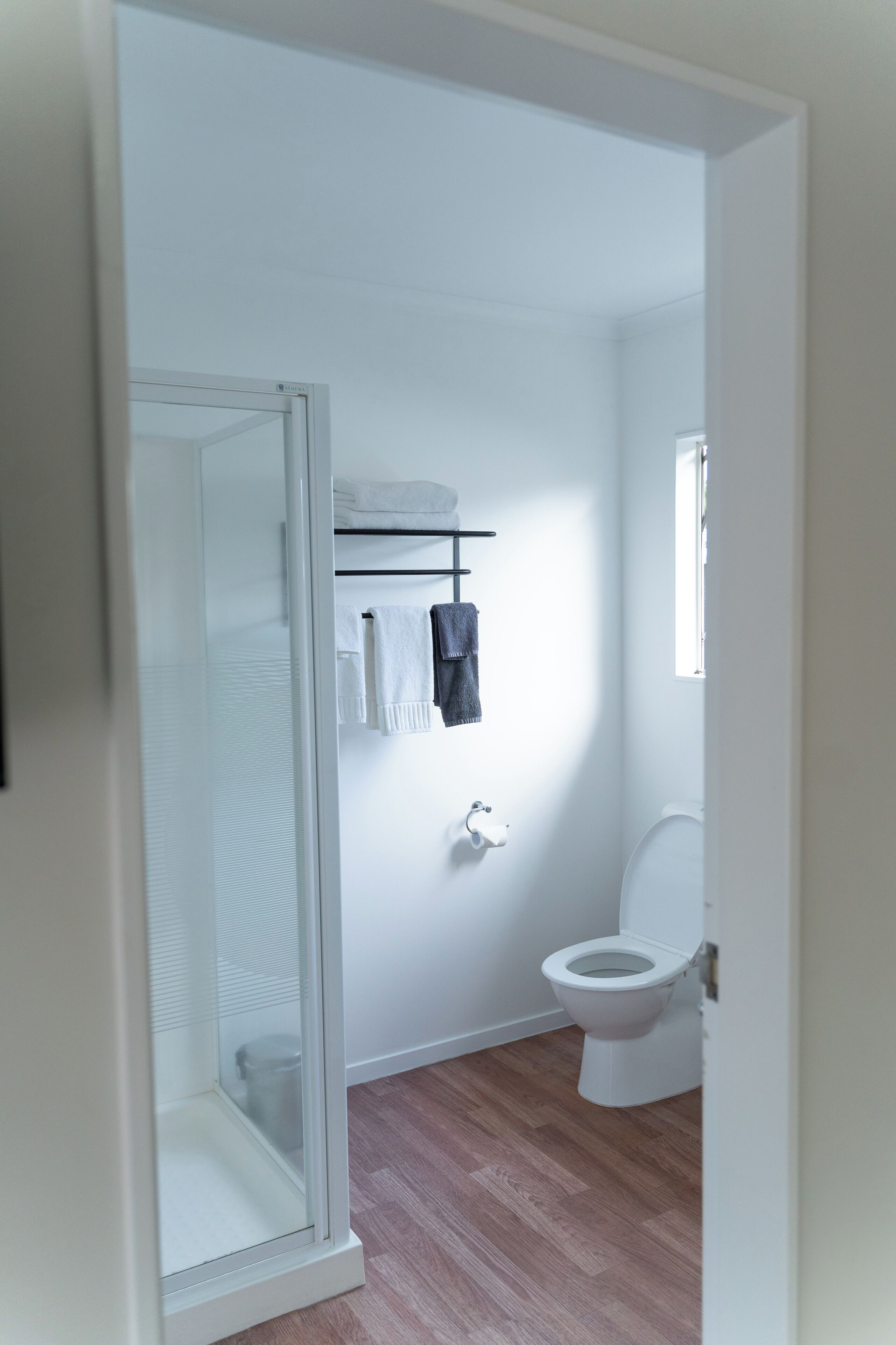 A bathroom with a glass shower enclosure, a white toilet, and a towel rack with towels.