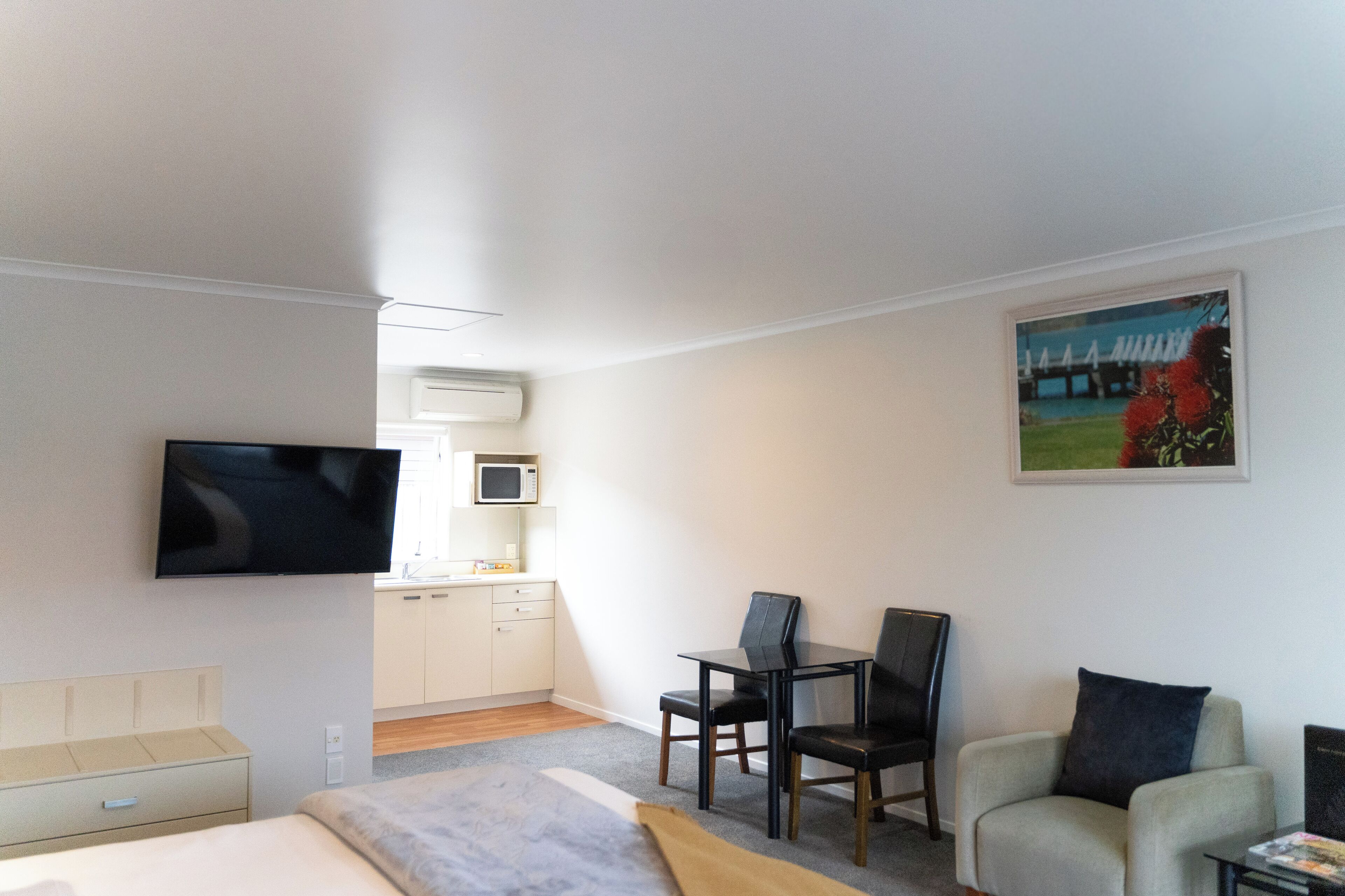 A hotel room with a bed, a desk, a chair, a television, a microwave, and a painting on the wall.