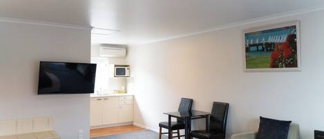 A hotel room with a bed, a desk, a chair, a television, a microwave, and a painting on the wall.