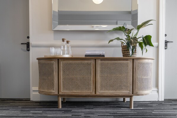 Una consola de madera con paneles de ratán, una planta en maceta y varios objetos decorativos encima.
