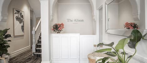 A reception area with a white reception desk, a staircase, and a large mirror.