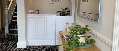 A hallway with a black and white striped carpet, a white reception desk, a mirror, and a sign that reads "The Alison".