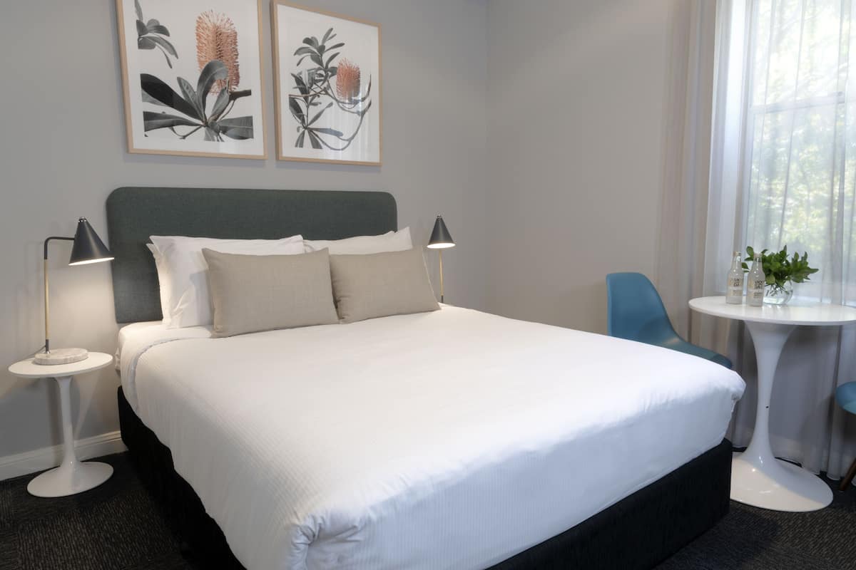 A neatly made bed with white linens, a dark headboard, and two bedside lamps. There are two framed botanical prints on the wall above the bed.