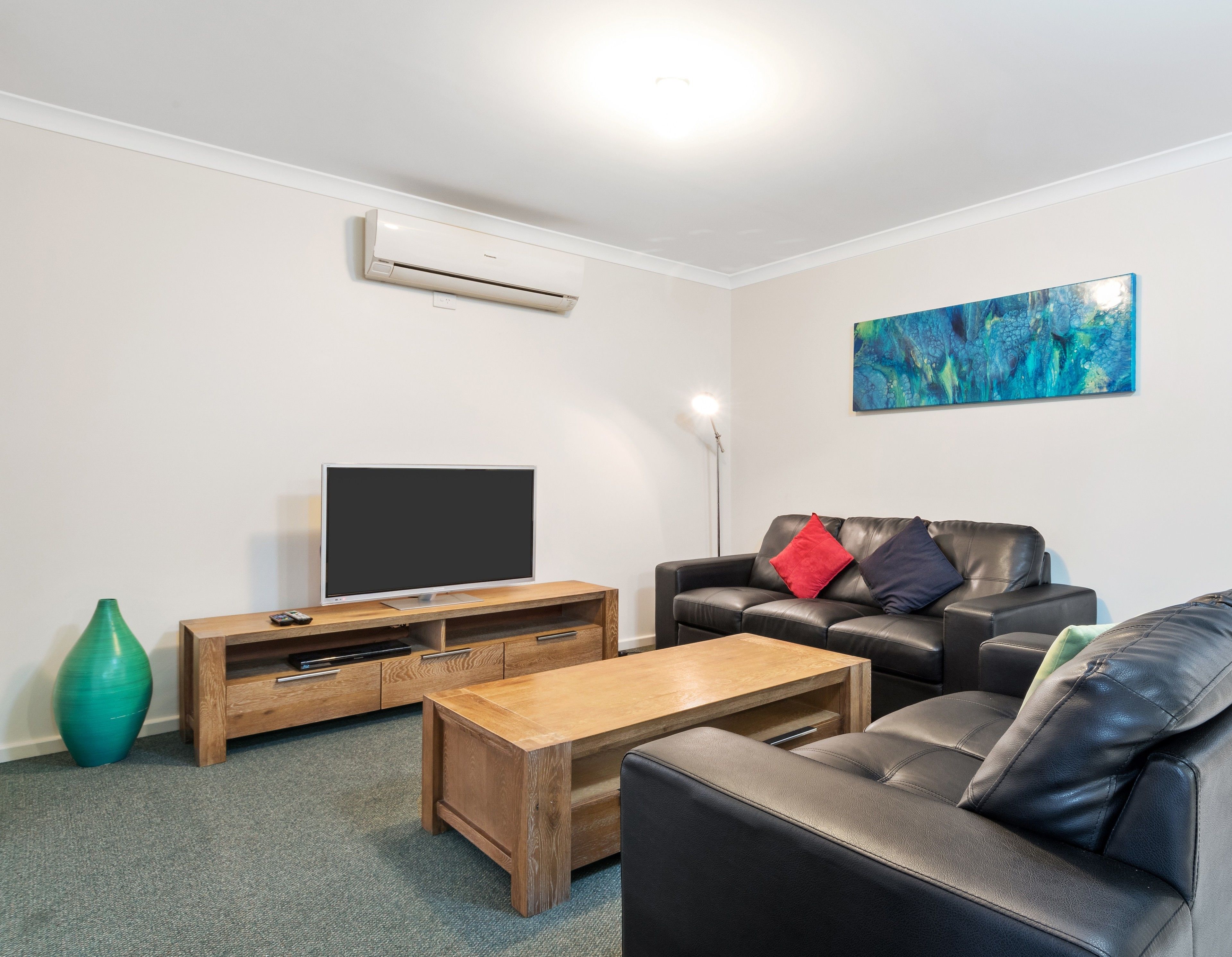 A modern living room with a flat-screen TV, leather sofa, wooden coffee table, and a painting on the wall.