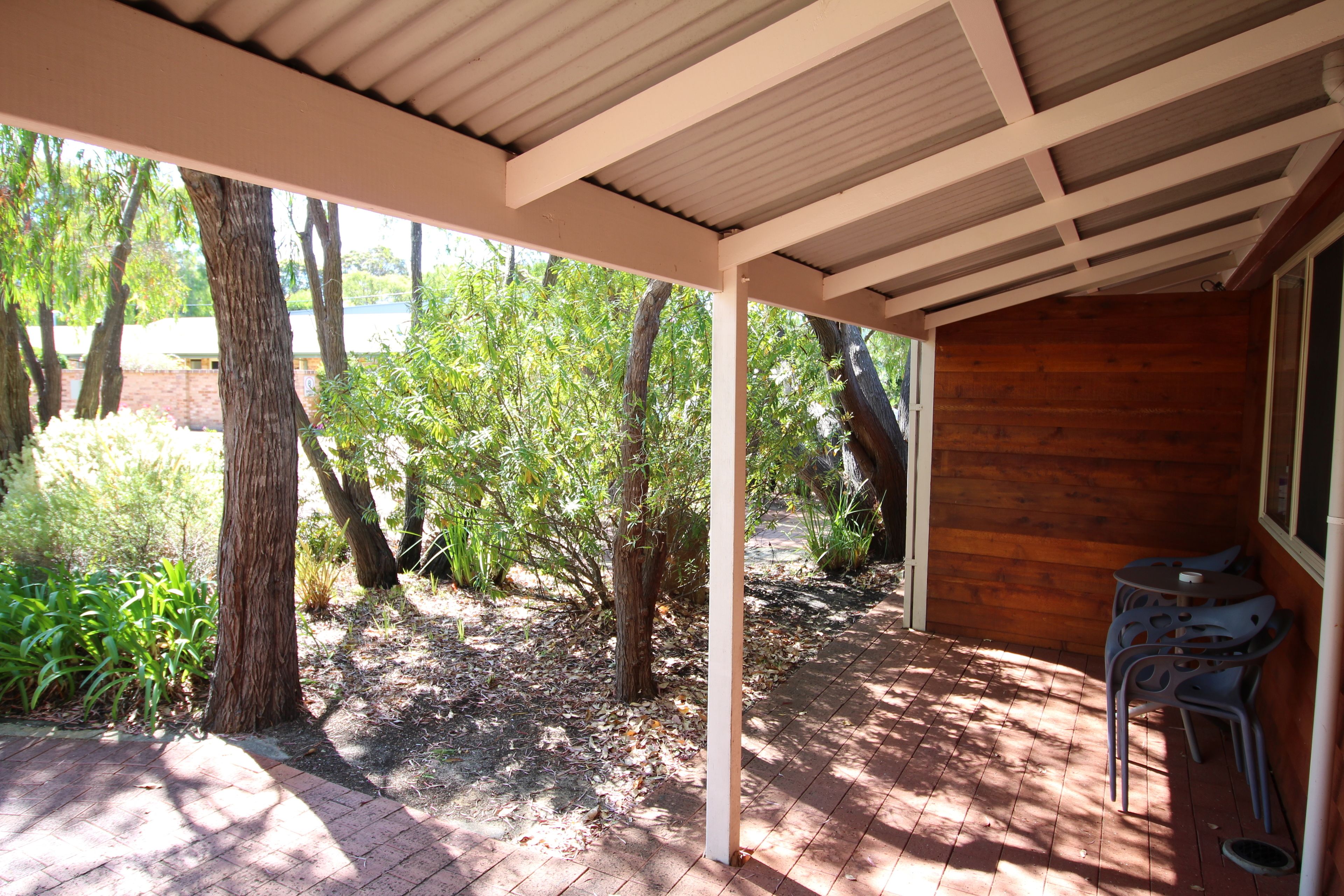A covered patio with a brick floor, wooden walls, and a view of a garden with trees and plants.