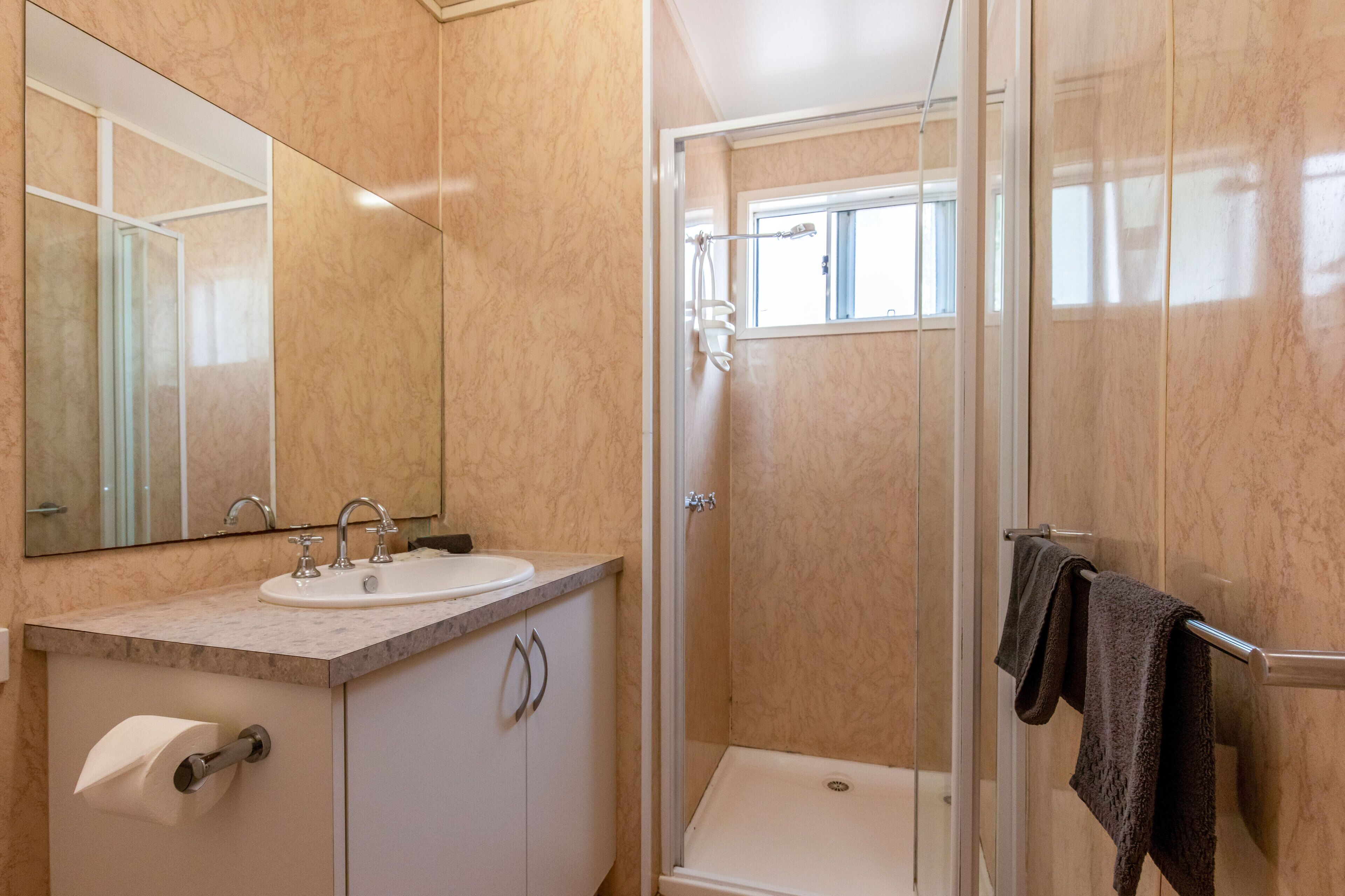 A bathroom with a sink, mirror, toilet paper holder, shower, and towel rack.