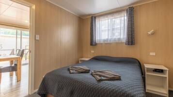 A bedroom with a bed, a window with curtains, a bedside table, and a chair visible through an open door.