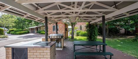 Un espace extérieur abrité comprenant un barbecue, une table de pique-nique et un mur en briques.