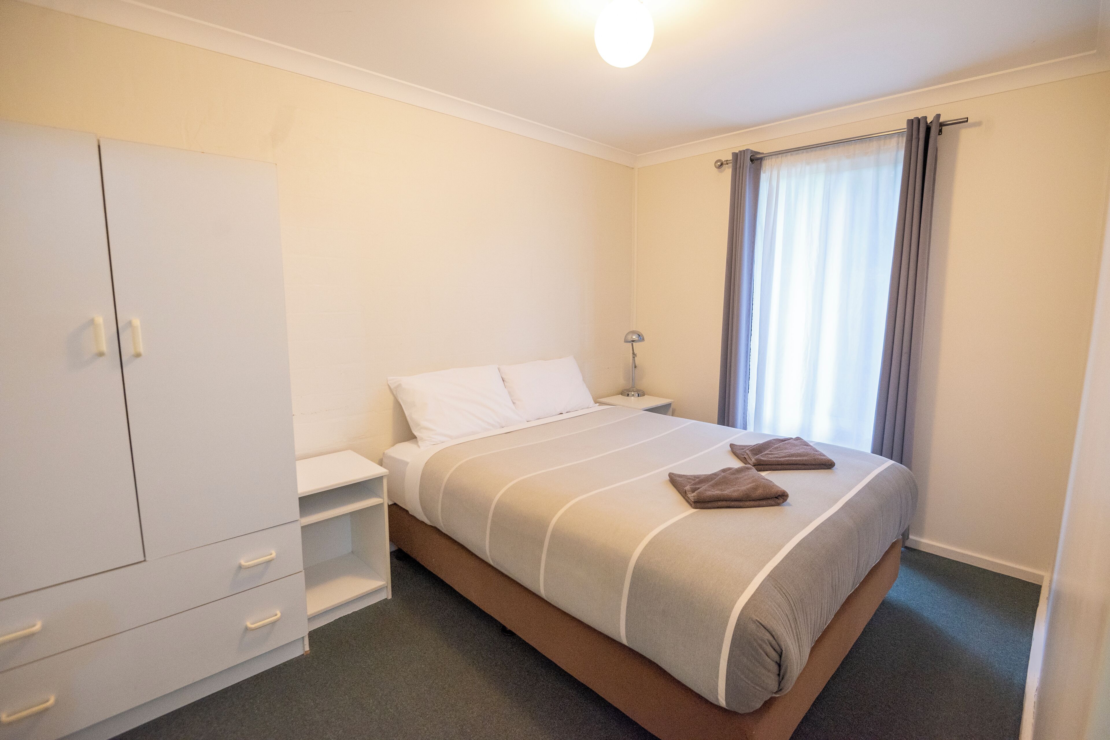 A hotel room with a bed, a wardrobe, a nightstand, and a window with curtains.