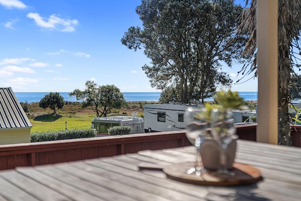 A balcony with a view of the sea, a glass of water, and a small table. - Tasman Holiday Parks - Ohiwa (Opotiki)