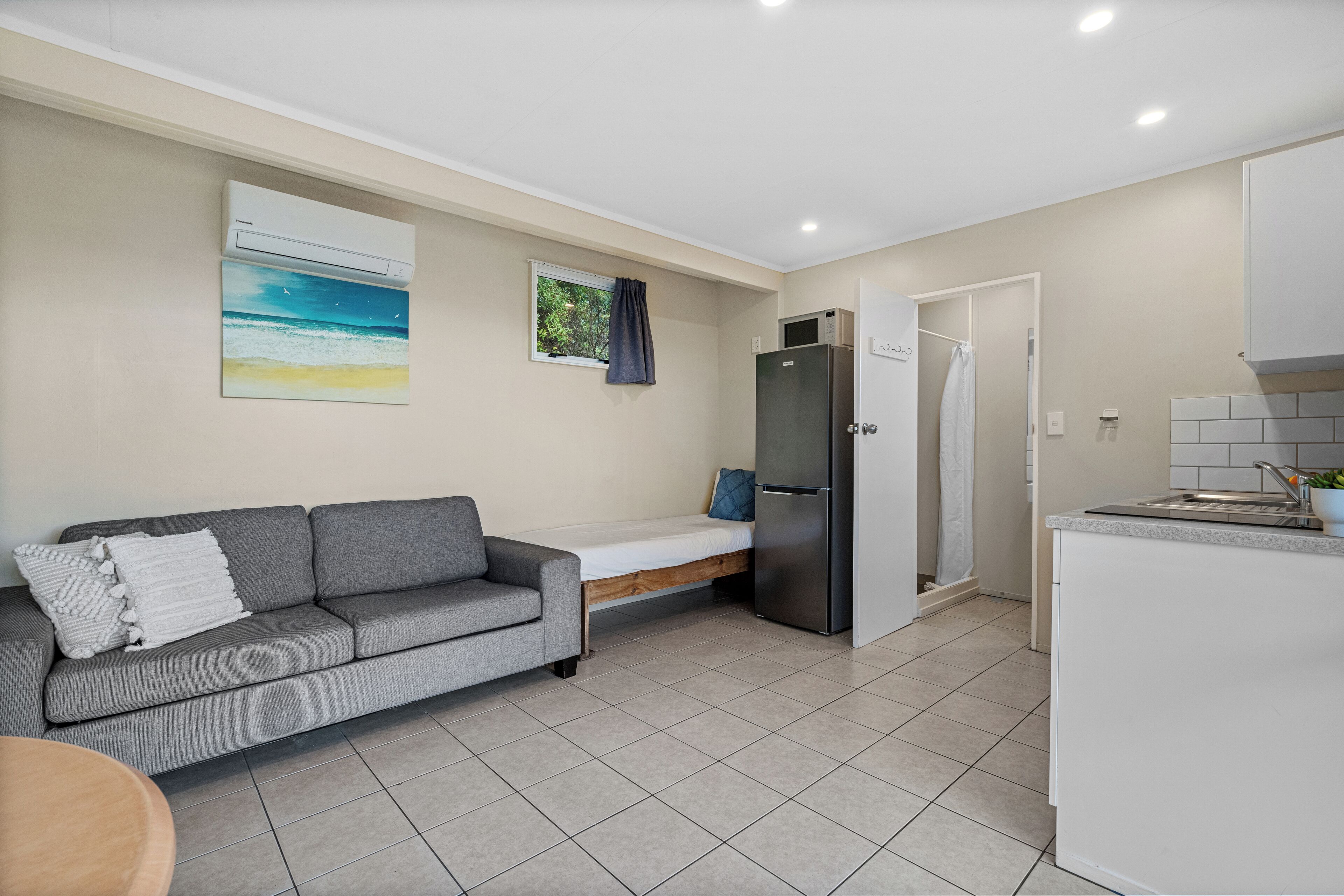 Un espacio habitable compacto con sofá, cama pequeña, refrigerador y kitchenette.