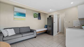 Un espacio habitable compacto con sofá, cama pequeña, refrigerador y kitchenette.