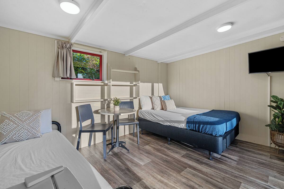 Een kleine kamer met een bed, een tafeltje, een stoel en een raam met gordijnen.