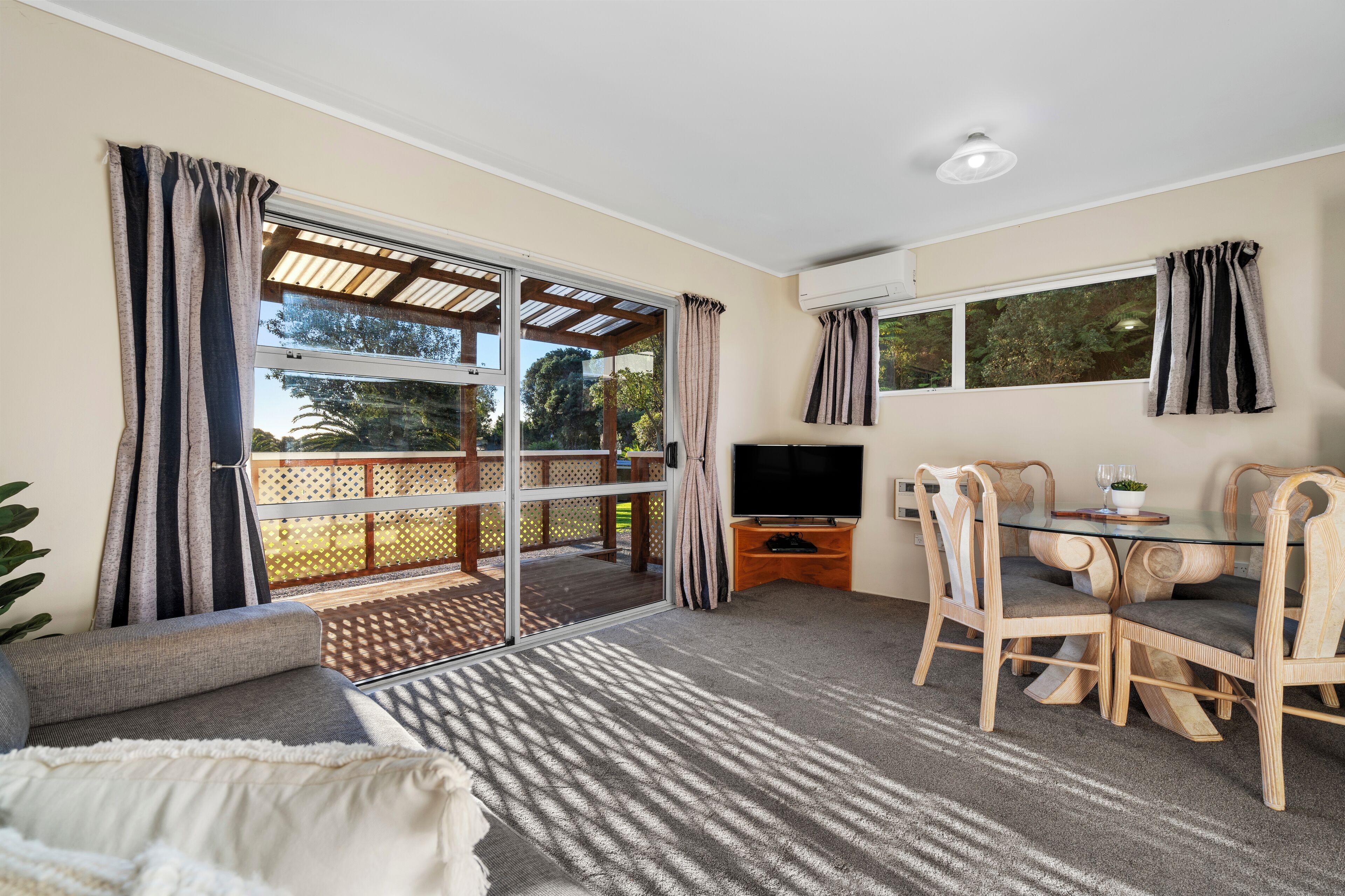 A room with a sofa, a glass table with chairs, a TV, and a view of the outdoors.