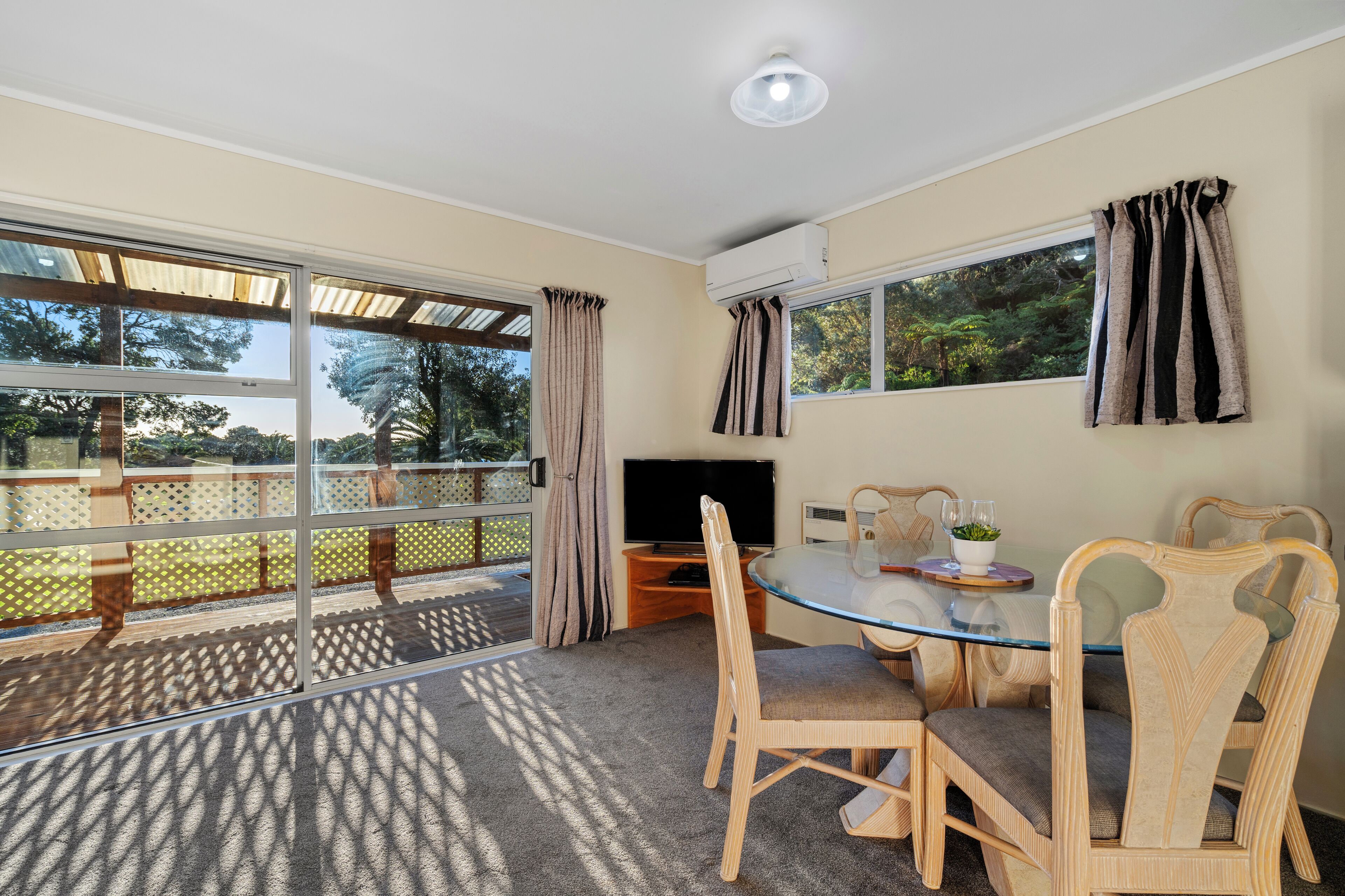 A room with a glass dining table, wicker chairs, a flat-screen TV, and a large window with curtains.