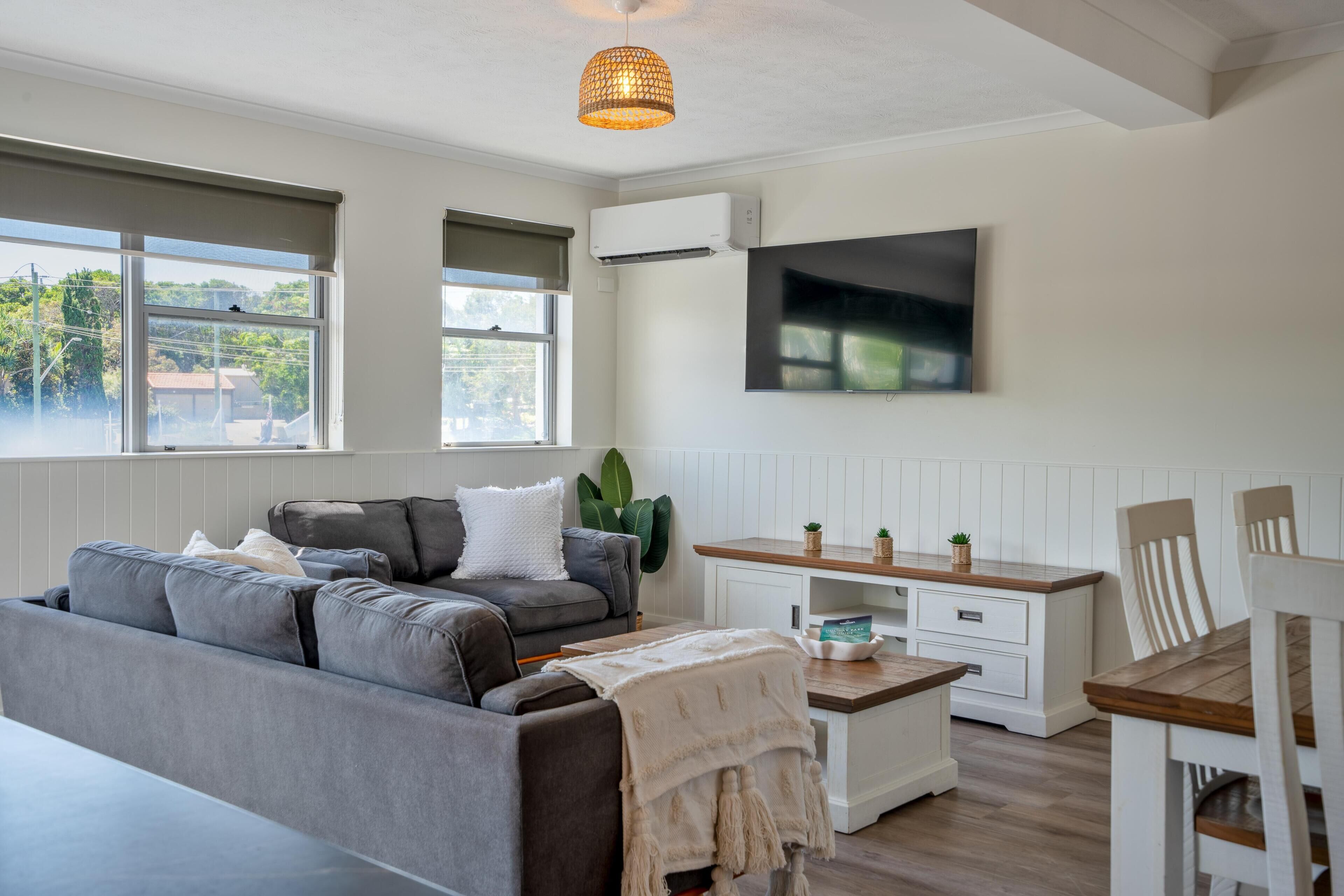 Una sala de estar moderna con un sofá gris, una mesa de centro de madera, un mueble blanco y un televisor montado en la pared.