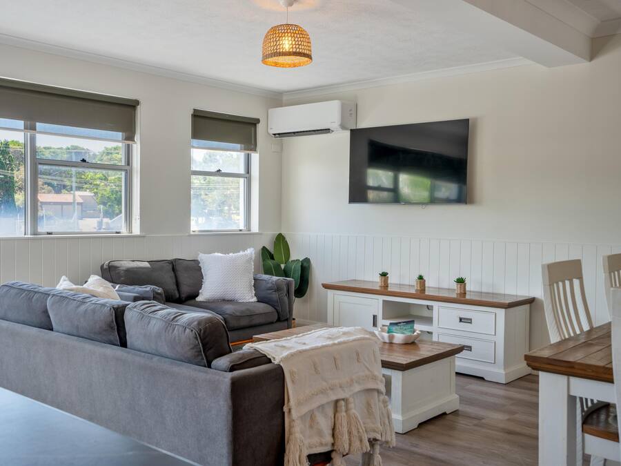 Una sala de estar moderna con un sofá gris, una mesa de centro de madera, un mueble blanco y un televisor montado en la pared.