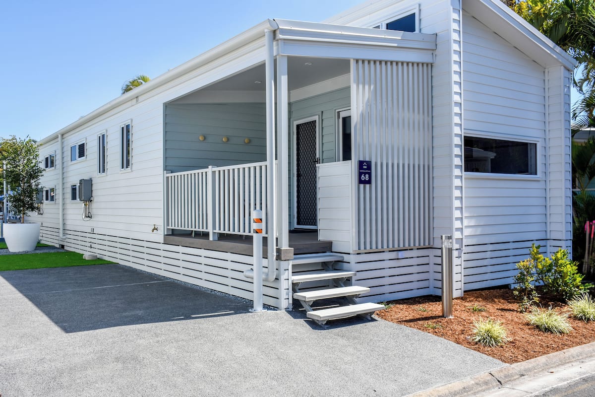 A white mobile home with a covered porch and a small front yard.