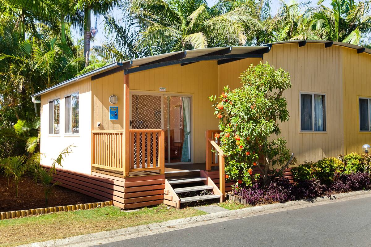 A single-story mobile home with a porch, a small front yard, and a palm tree in the background.