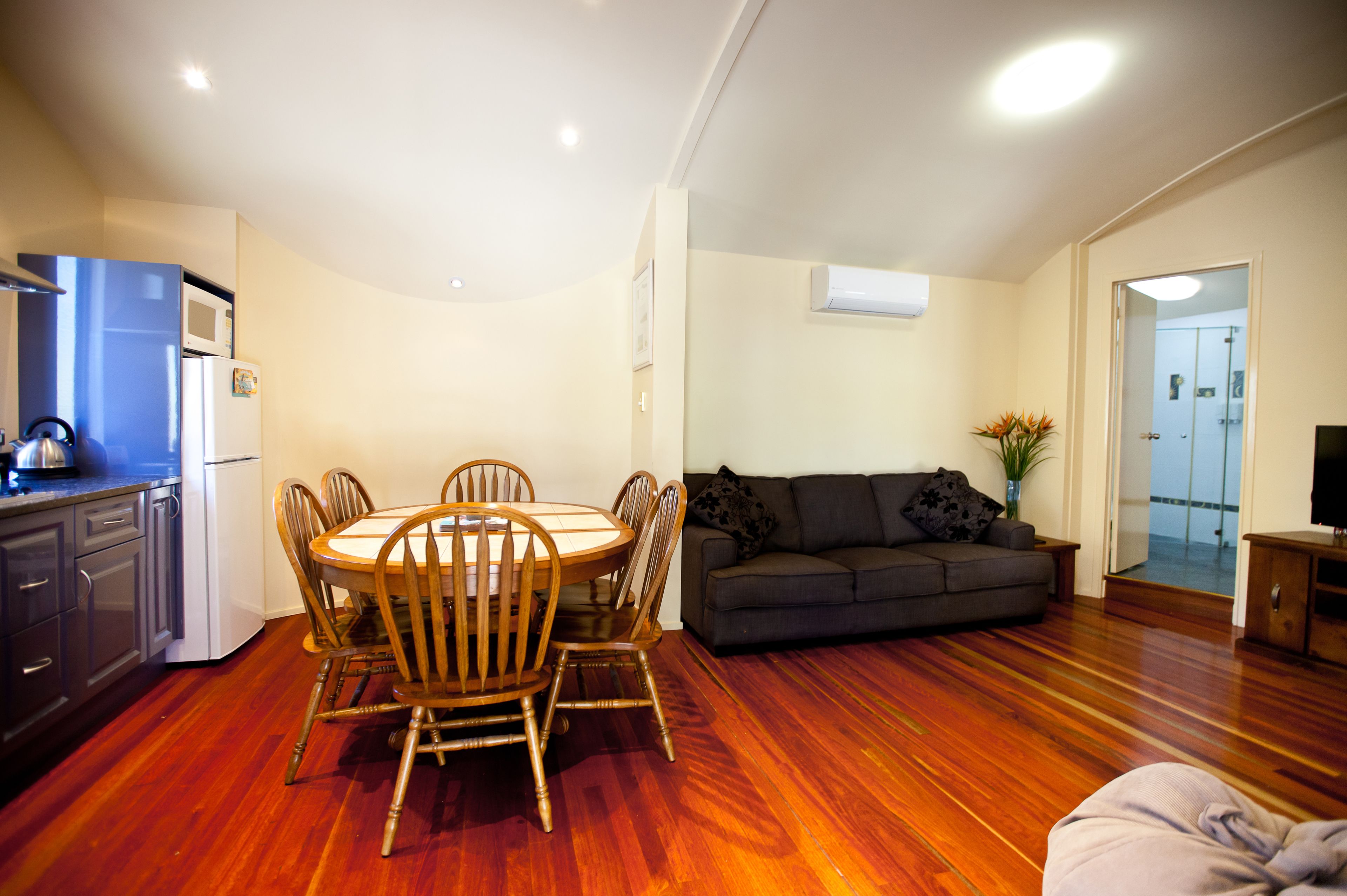 A living room with a dining table and chairs, a sofa, and a kitchen area with a refrigerator and microwave.