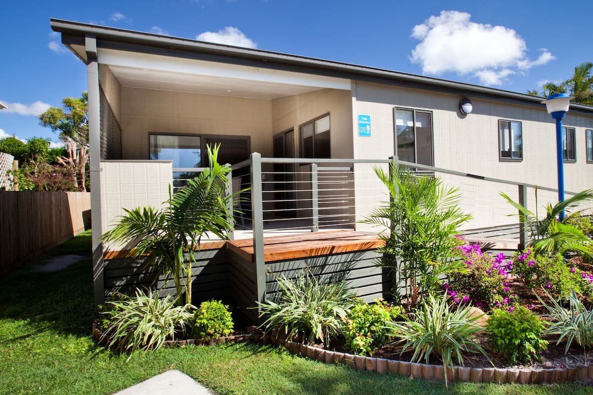 A modern two-story house with a covered porch, a fenced backyard, and various plants and shrubs.