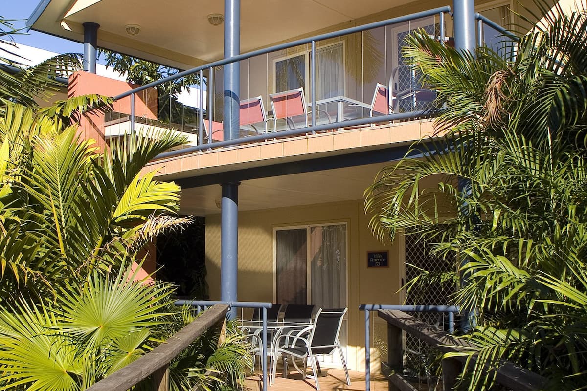 A two-story building with a balcony, palm trees, and outdoor seating.