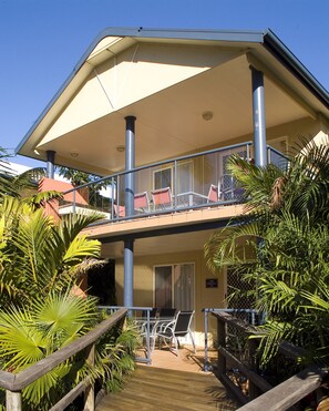 A two-story building with a balcony, palm trees, and outdoor seating.
