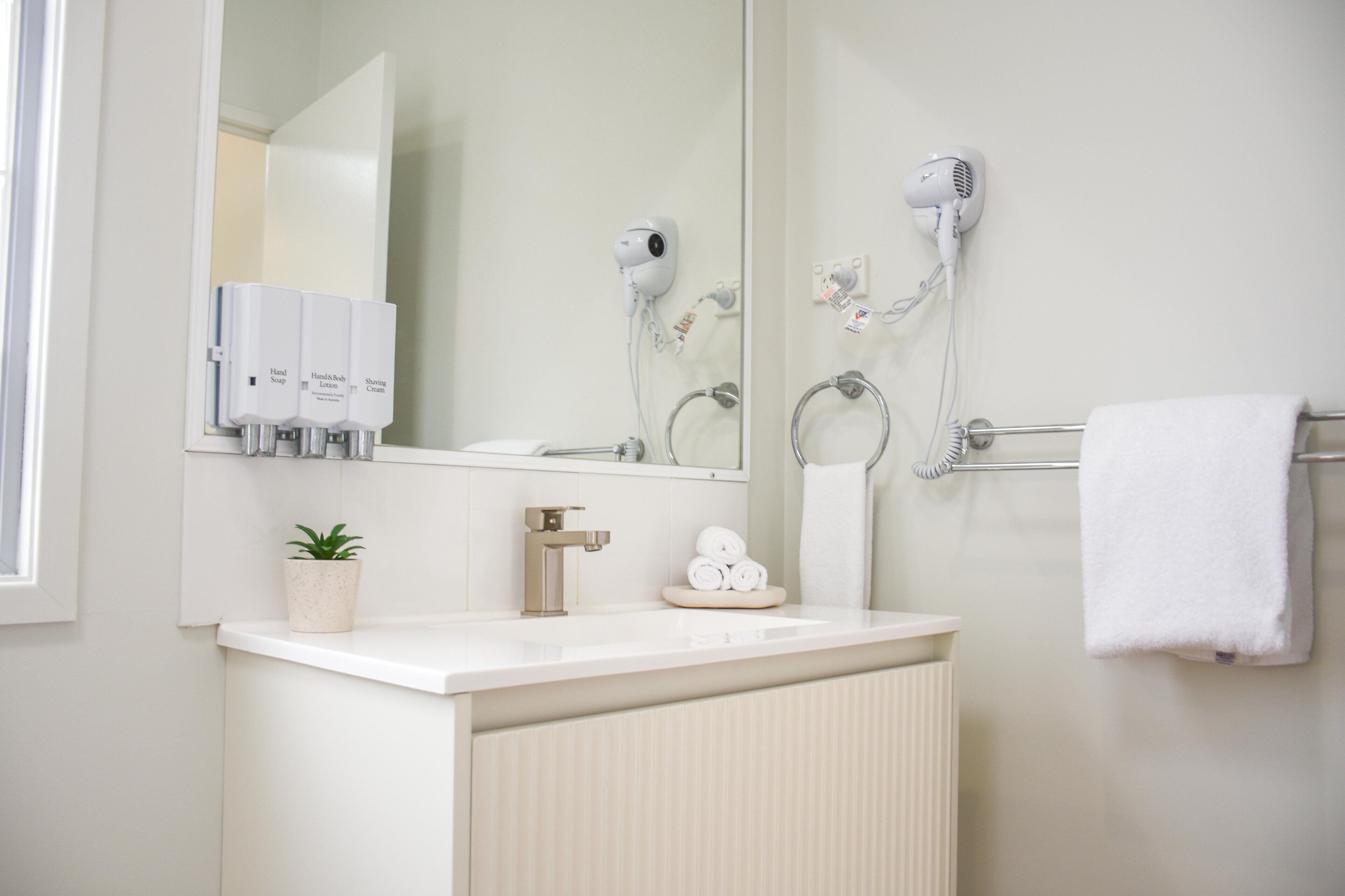 Un bany amb un lavabo, mirall, paraigua i assecador de cabells.