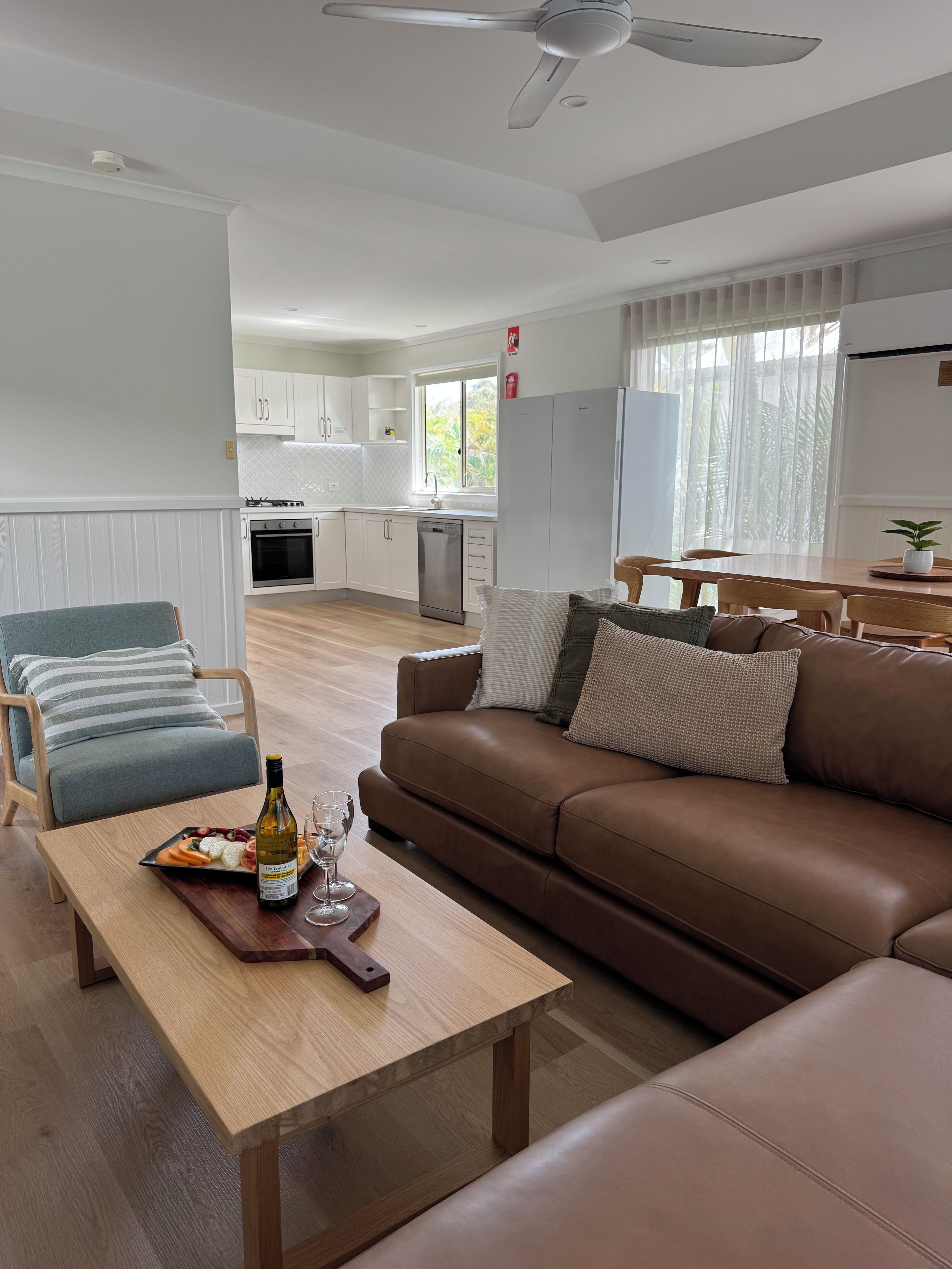 A modern living room with a brown leather sofa, a wooden coffee table with a bottle and glasses, and a grey armchair.