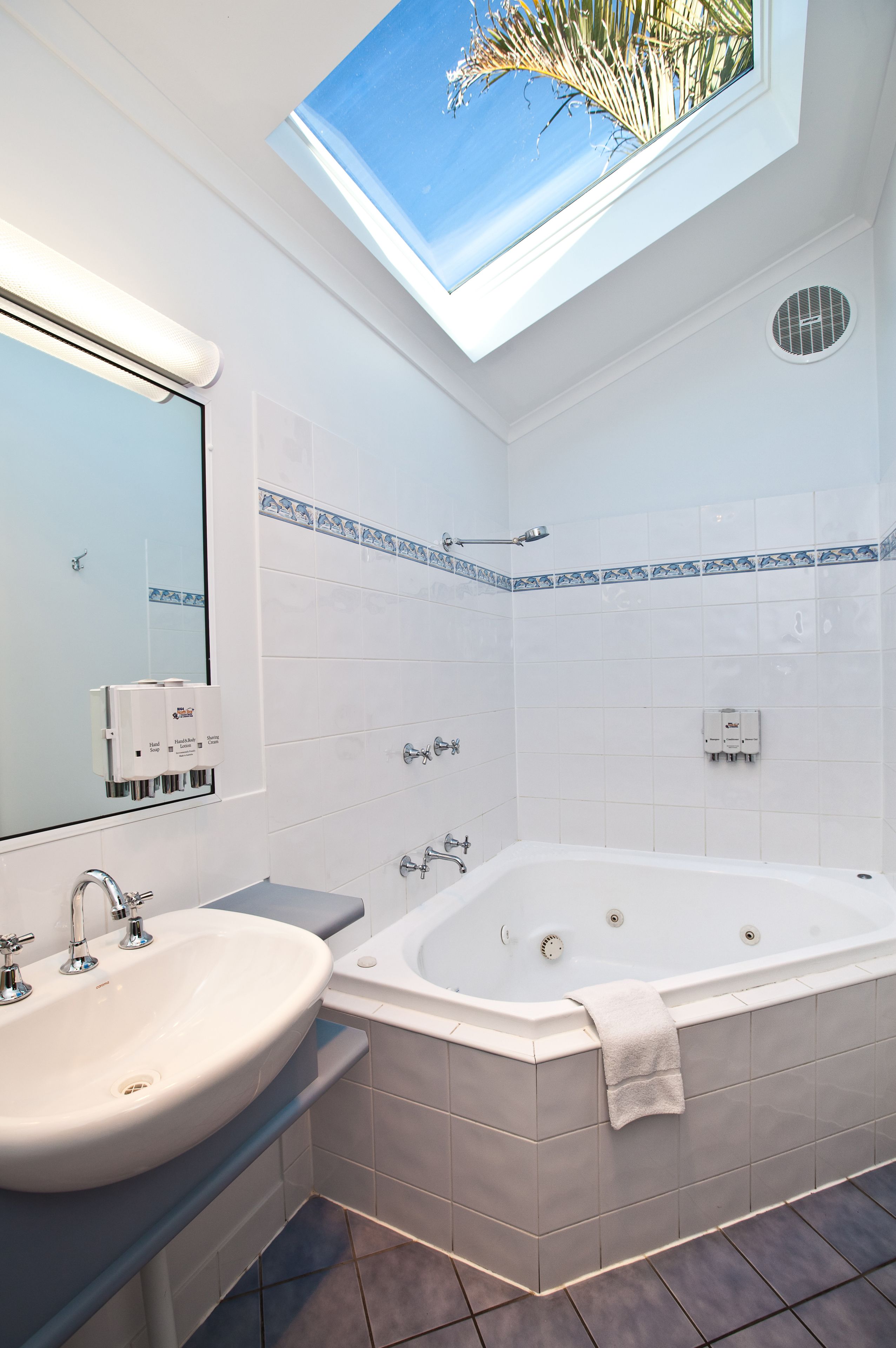 Un baño moderno con tragaluz, una bañera grande, un lavabo y un espejo.