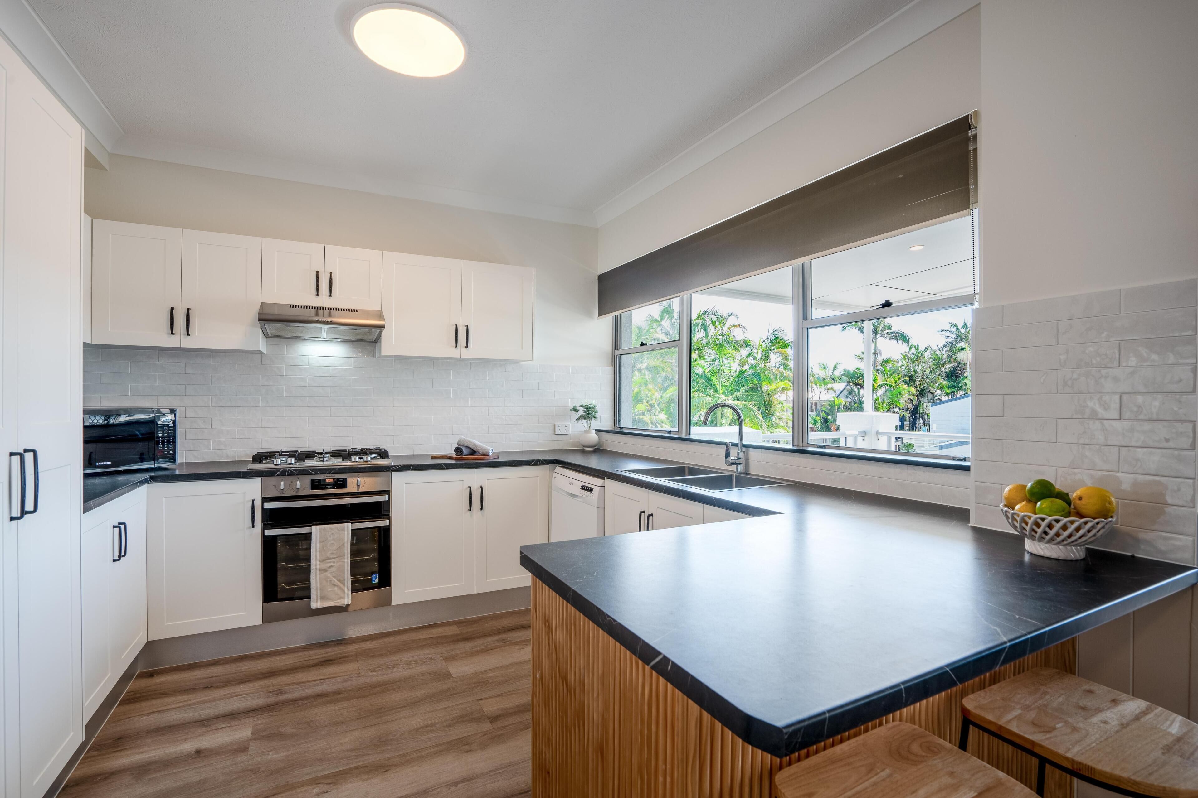 A modern kitchen with white cabinets, a black countertop, a built-in oven, and a window with a view of greenery.