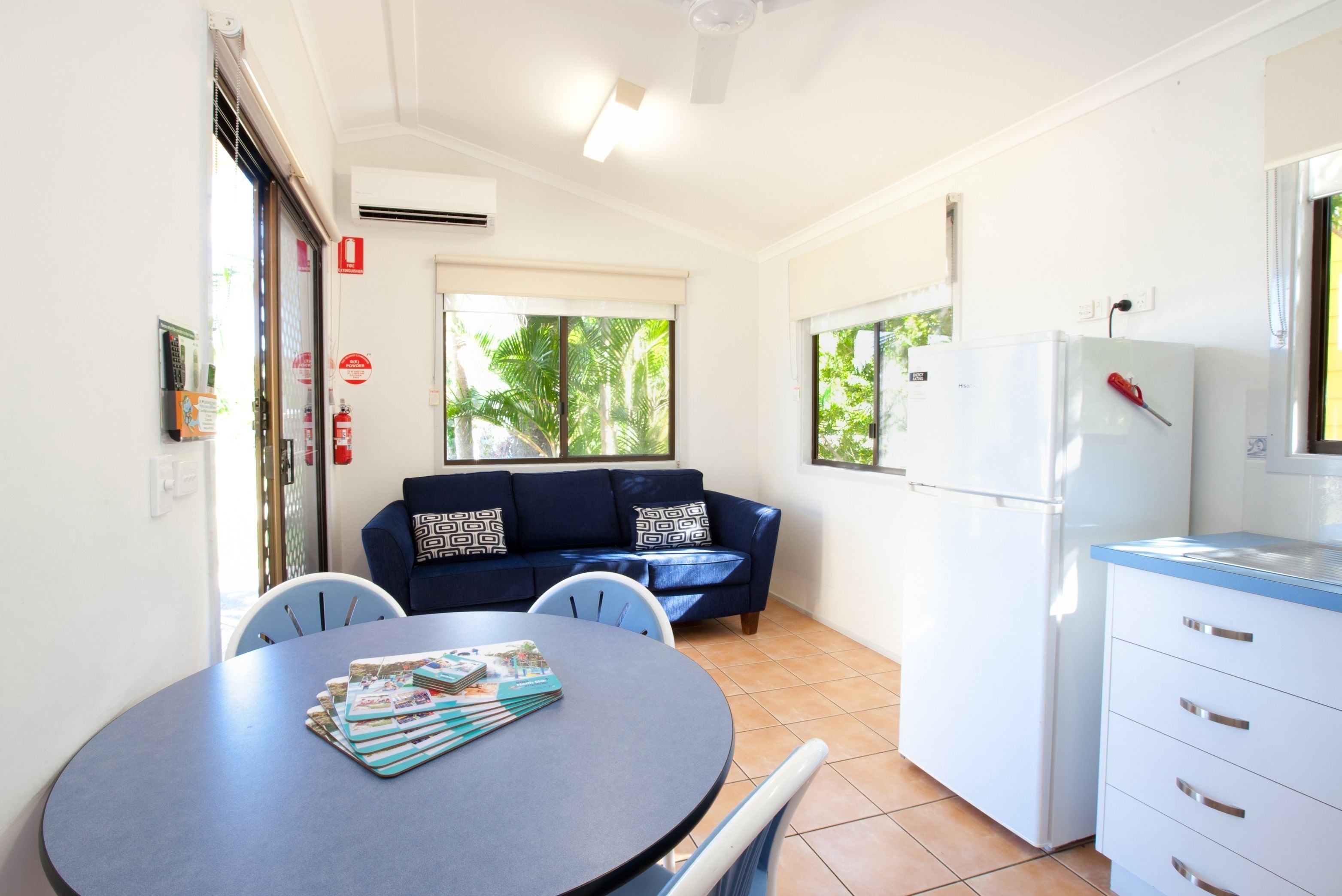A compact kitchen with a dining area, a white refrigerator, and a blue sofa with patterned cushions.