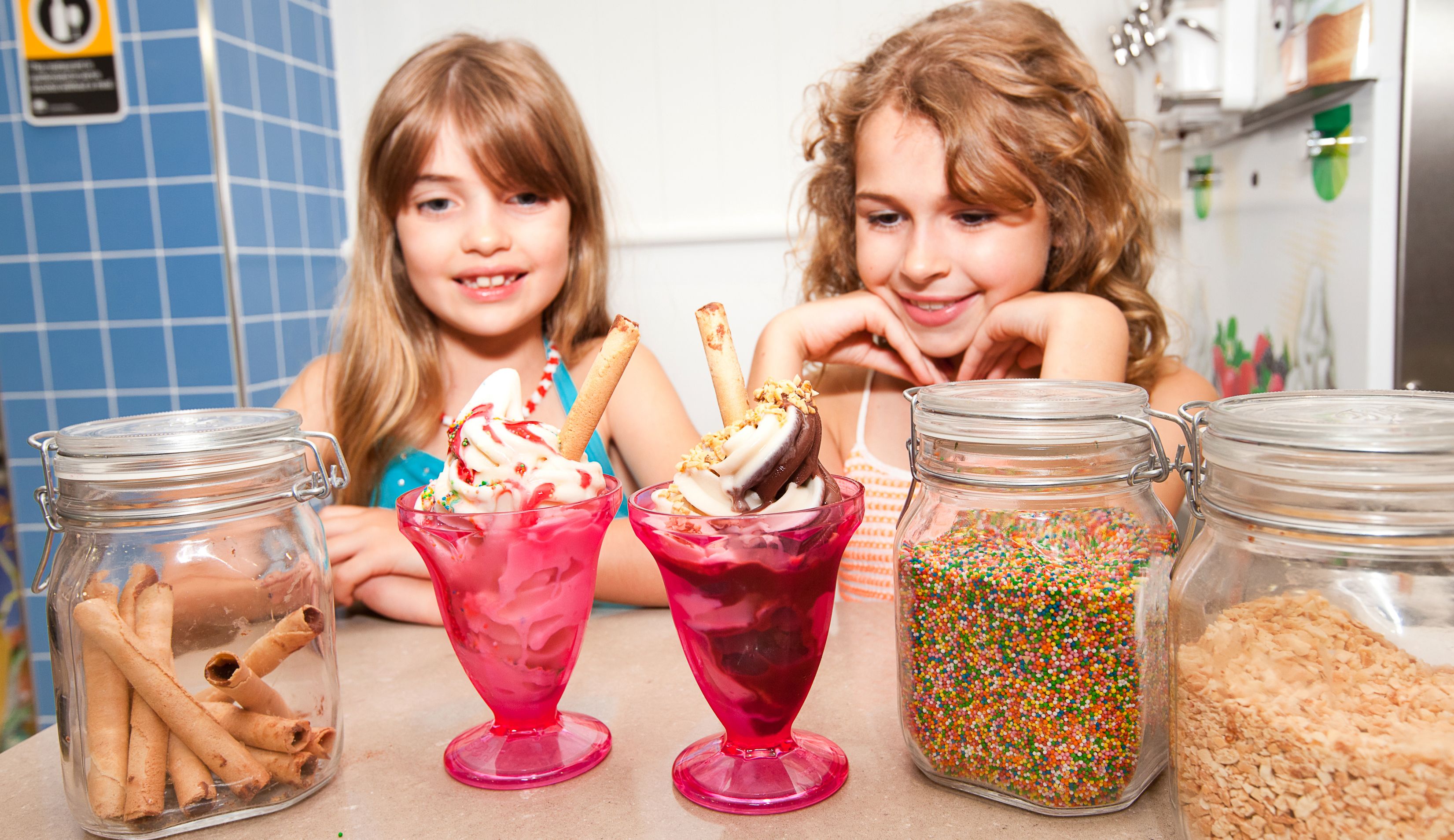 Two children sitting at a table with colorful desserts and jars of ingredients.