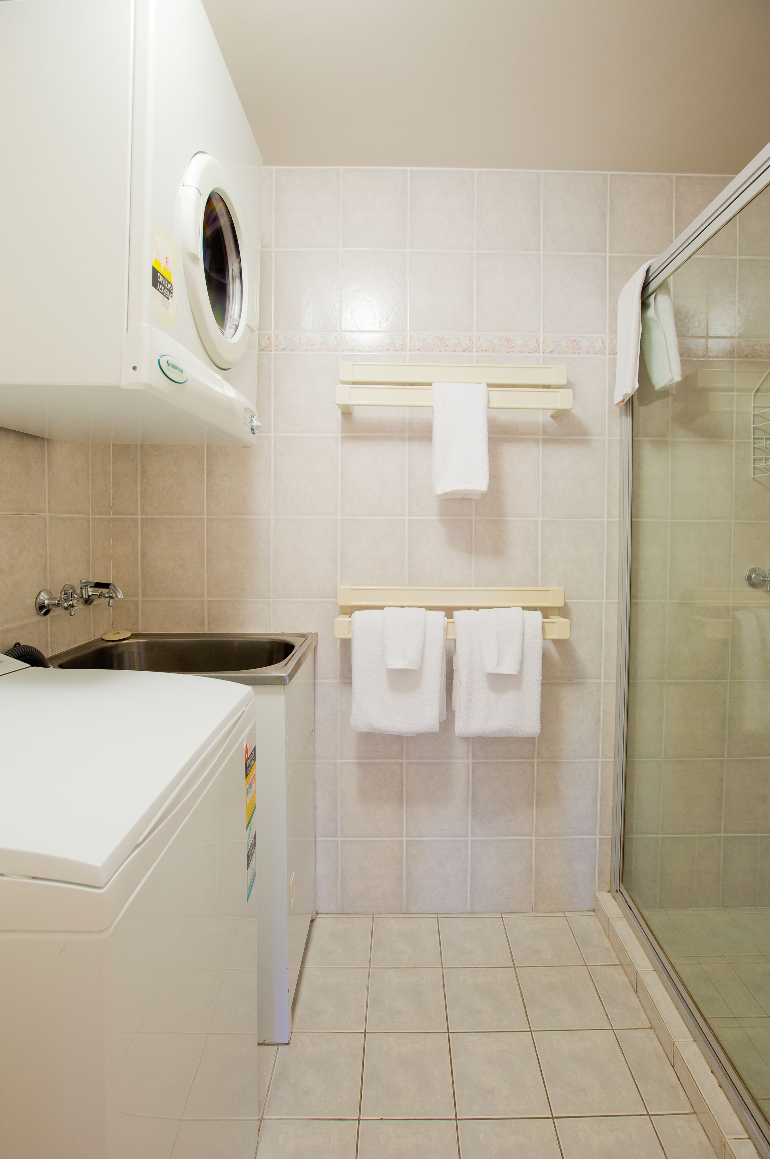 A bathroom with a washing machine, a sink, a glass shower enclosure, and a towel rack with towels.