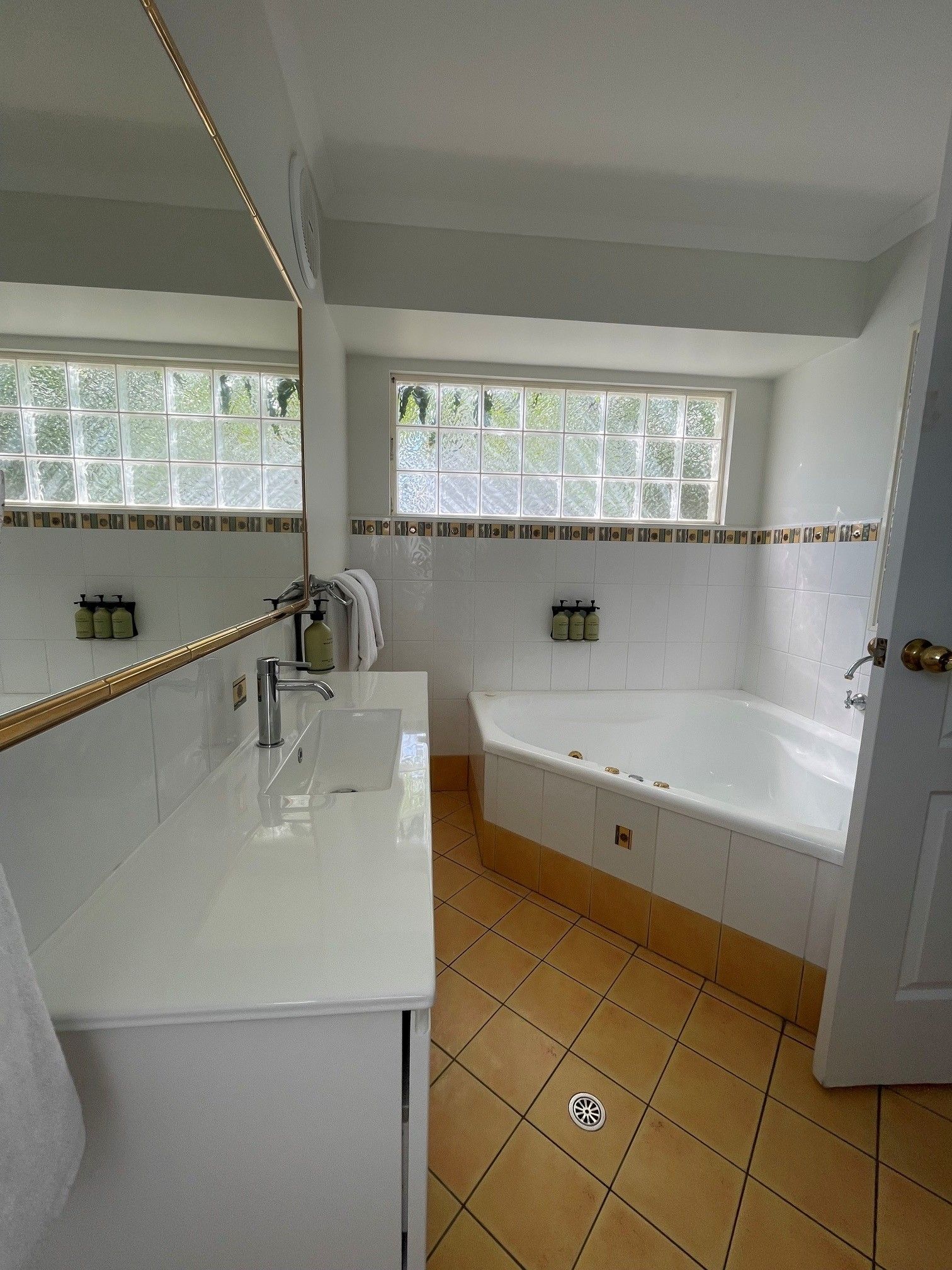 Une salle de bain avec un lavabo blanc, une baignoire et une fenêtre donnant sur un paysage verdoyant.