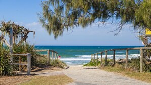 A coastal pathway leading to the beach with a wooden fence and a lifeguard tower in the background. - La Grande Apartments Broadbeach (Broadbeach)
