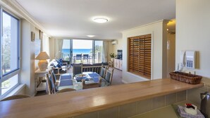 A dining area with a view of the ocean, a kitchen with a wooden countertop, and a seating area with a table and chairs. - La Grande Apartments Broadbeach (Broadbeach)