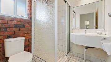 Une salle de bain comprenant des toilettes, une douche avec une porte en verre, un lavabo et un miroir.