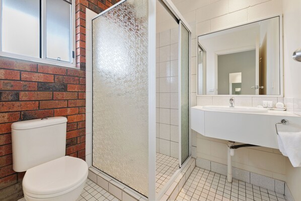 Un baño con inodoro, ducha con puerta de vidrio, lavabo y espejo.
