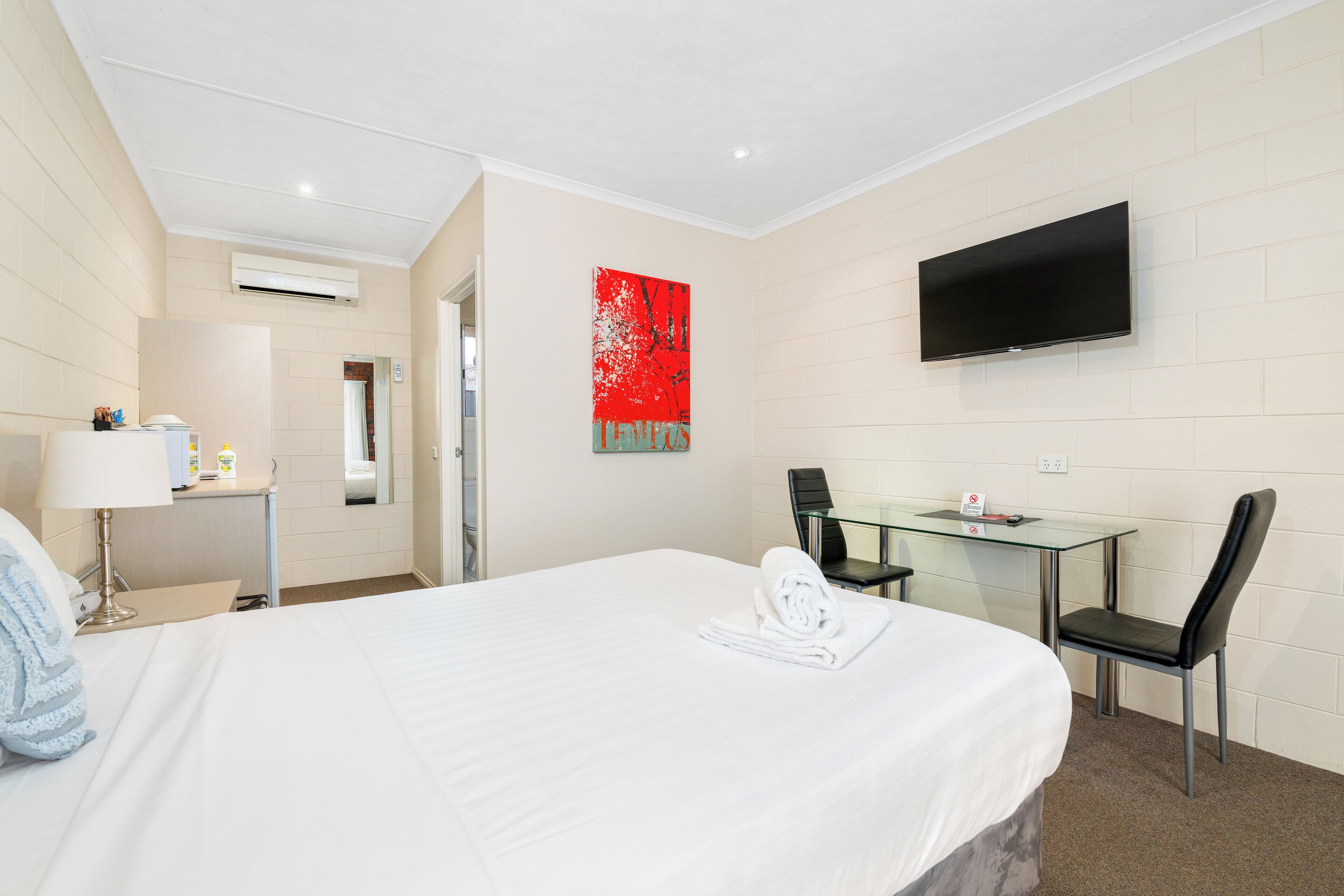 Une chambre d’hôtel avec un lit, un bureau, une chaise, une télévision et un tableau abstrait rouge accroché au mur.