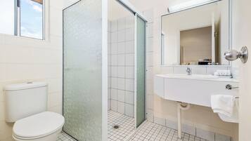 Une salle de bain comprenant des toilettes, une douche à parois de verre, un lavabo et un miroir.