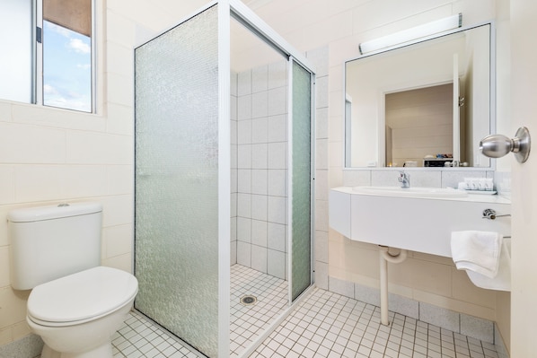 Un baño con inodoro, cabina de ducha de vidrio, lavabo y espejo.