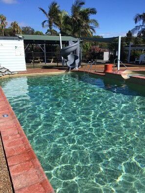 A clear pool with a diving board, surrounded by palm trees and a covered seating area. - Diamond Beach Holiday Park (Diamond Beach)