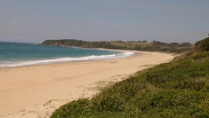 A beach with clear blue water, sandy shore, and grassy hills in the background. - Diamond Beach Holiday Park (Diamond Beach)