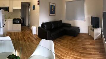 A compact living space with a kitchenette, a black leather sofa, a glass dining table, and a television.