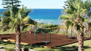 A view of a beach with palm trees, a swing set, and a clear blue ocean. - Diamond Beach Holiday Park (Diamond Beach)