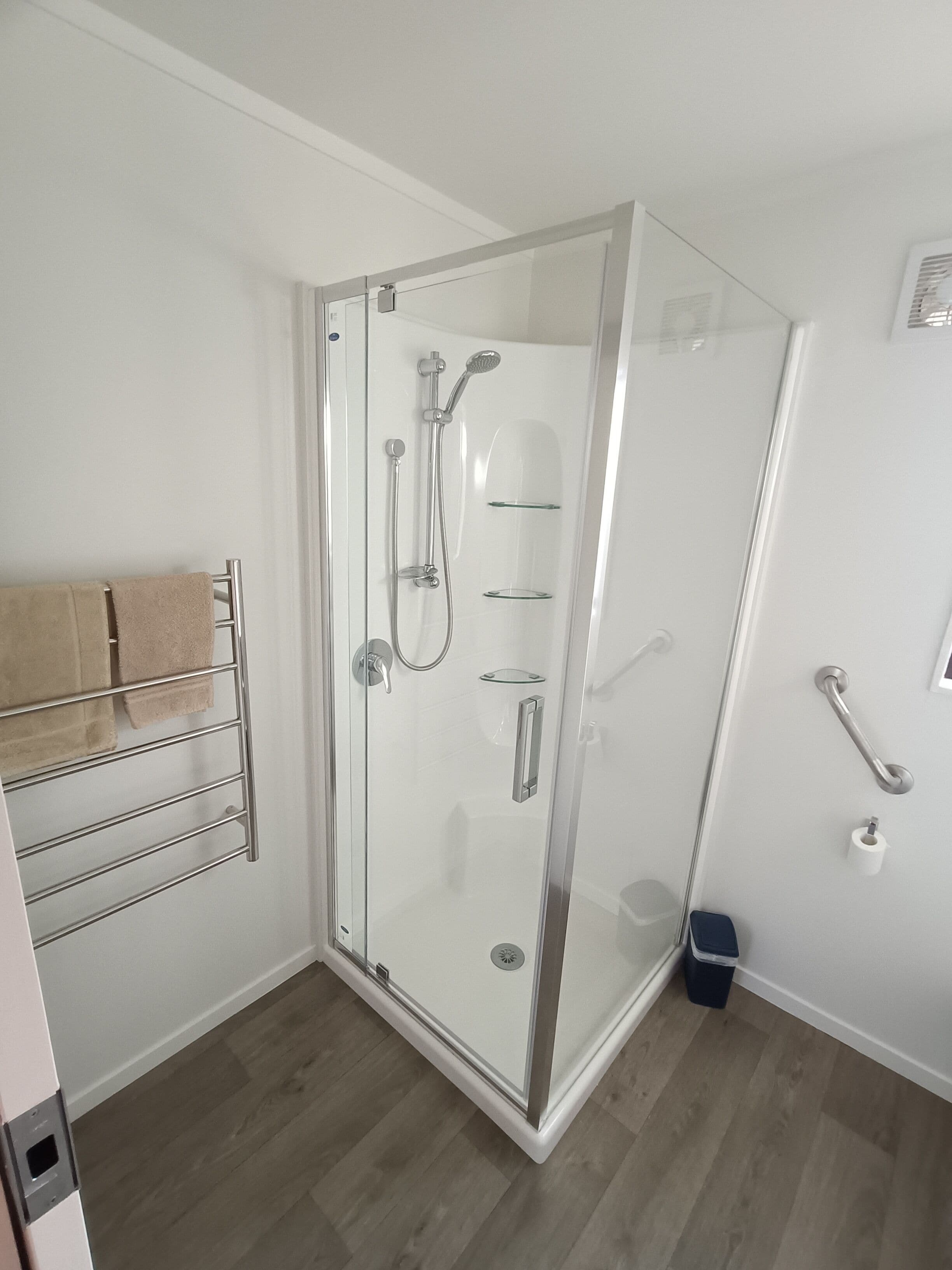 Ein modernes Badezimmer mit einer in Glas abgeschlossenen Dusche, einem Handtuchhalter mit Handtüchern und einer Haltestange.
