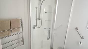 Ein modernes Badezimmer mit einer in Glas abgeschlossenen Dusche, einem Handtuchhalter mit Handtüchern und einer Haltestange.
